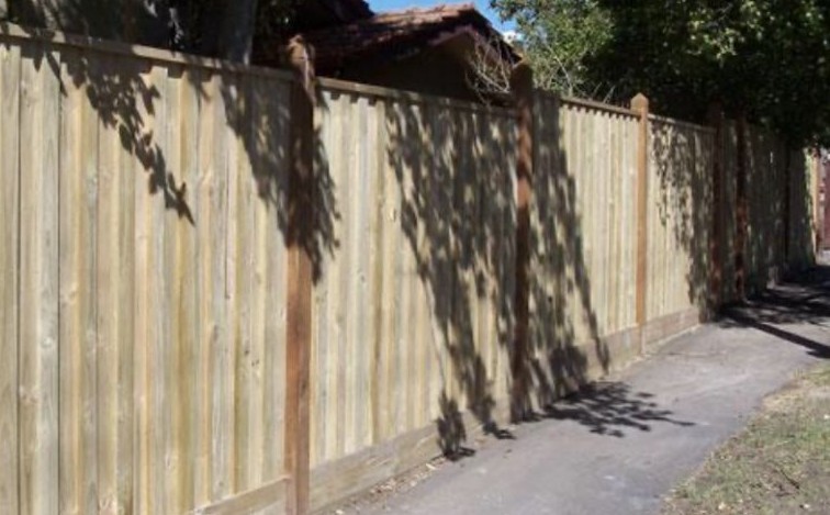 Treated pine timber paling fence with exposed posts along a footpath